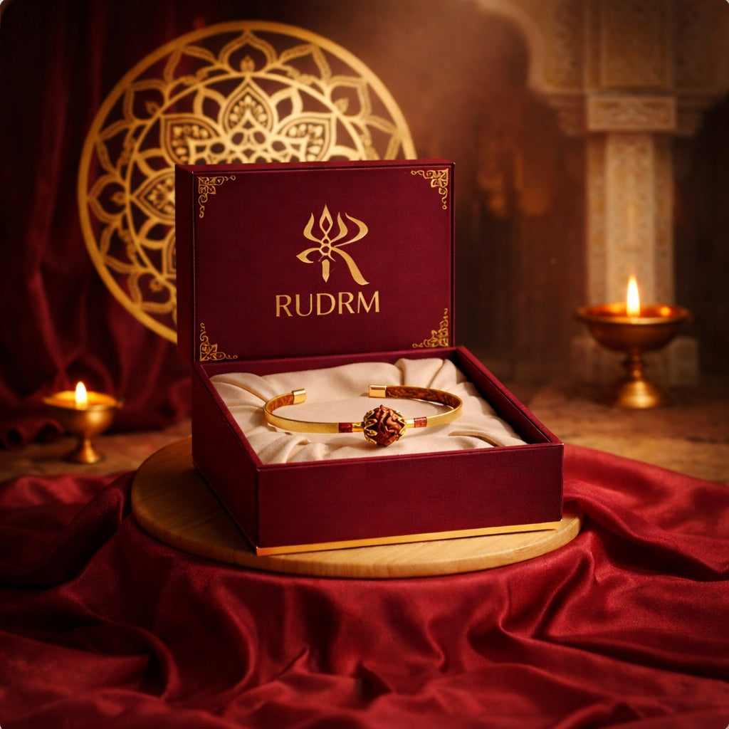Rudraksha bracelet and bangle displayed inside a maroon 'RUDRM' box, set against a golden mandala backdrop with lit oil lamps, creating a serene and spiritual atmosphere.