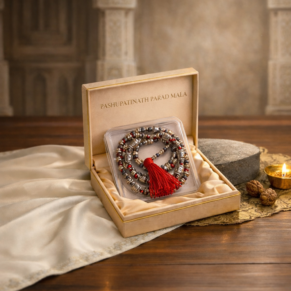 Pashupatinath Parad Mala with a red tassel, placed inside a luxurious box with the brand name, surrounded by a lit diya and decorative elements, set on a wooden table.