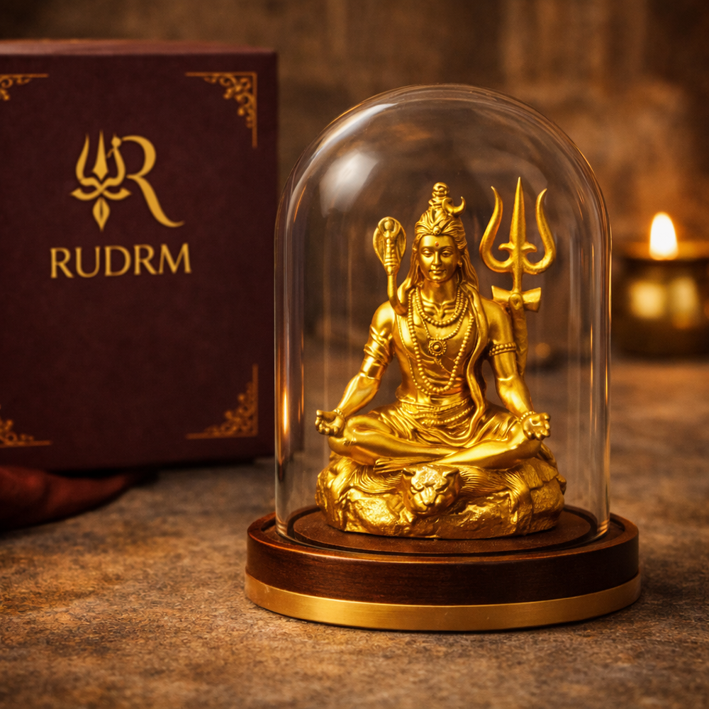 Golden statue of Lord Shiva under a glass dome, placed next to a 'Rudrm' branded box, with a lit diya in the background.