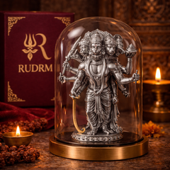 Silver statue of Lord Hanuman with multiple heads and arms under a glass dome, placed next to a 'Rudrm' branded box, with a lit diya and flower petals in the background.