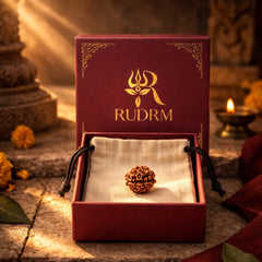 Rudraksha bead placed inside a velvet-lined box with the 'RUDRM' logo, accompanied by a lit oil lamp and marigold flowers, creating a spiritual ambiance.