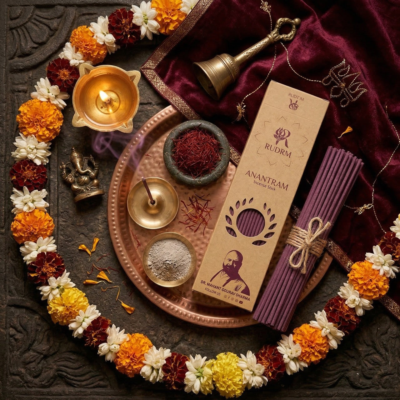 Rudrm Anantram incense sticks, flower garland, brass bell, incense holder, saffron, and incense smoke, set on a traditional metal plate with a Ganesha idol and velvet cloth, all surrounded by a serene ritualistic arrangement.