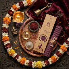 Rudrm Anantram incense sticks, flower garland, brass bell, incense holder, saffron, and incense smoke, set on a traditional metal plate with a Ganesha idol and velvet cloth, all surrounded by a serene ritualistic arrangement.