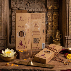 Orange Gauri incense sticks from Rudrm with incense smoke, a brass incense holder, a Rudrm incense box, a Rudraksha mala, and a lotus flower, set against an intricately carved stone background with golden highlights.