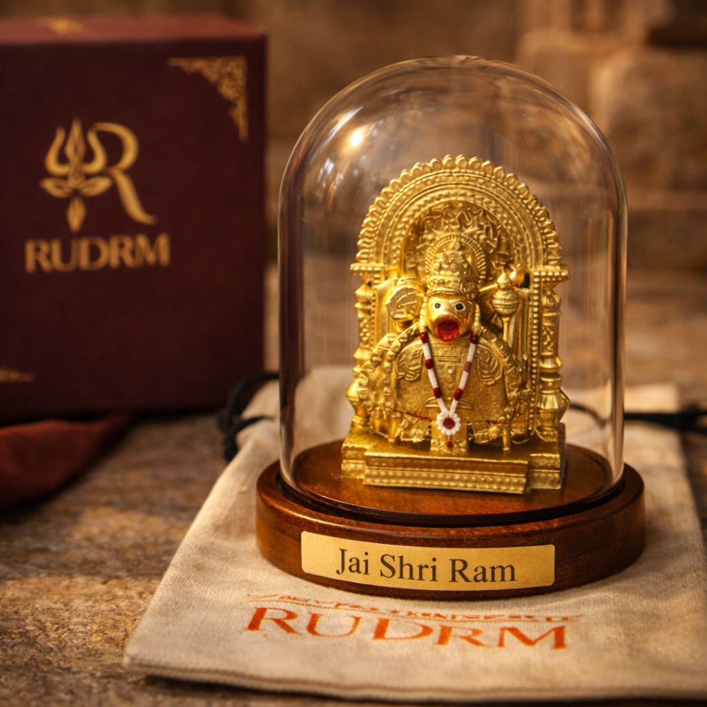 Golden statue of Lord Hanuman under a glass dome with a 'Jai Shri Ram' plaque, placed on a wooden base, next to a 'Rudrm' branded box, with a rudraksha mala in the background.