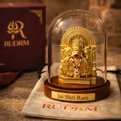 Golden statue of Lord Hanuman under a glass dome with a 'Jai Shri Ram' plaque, placed on a wooden base, next to a 'Rudrm' branded box, with a rudraksha mala in the background.