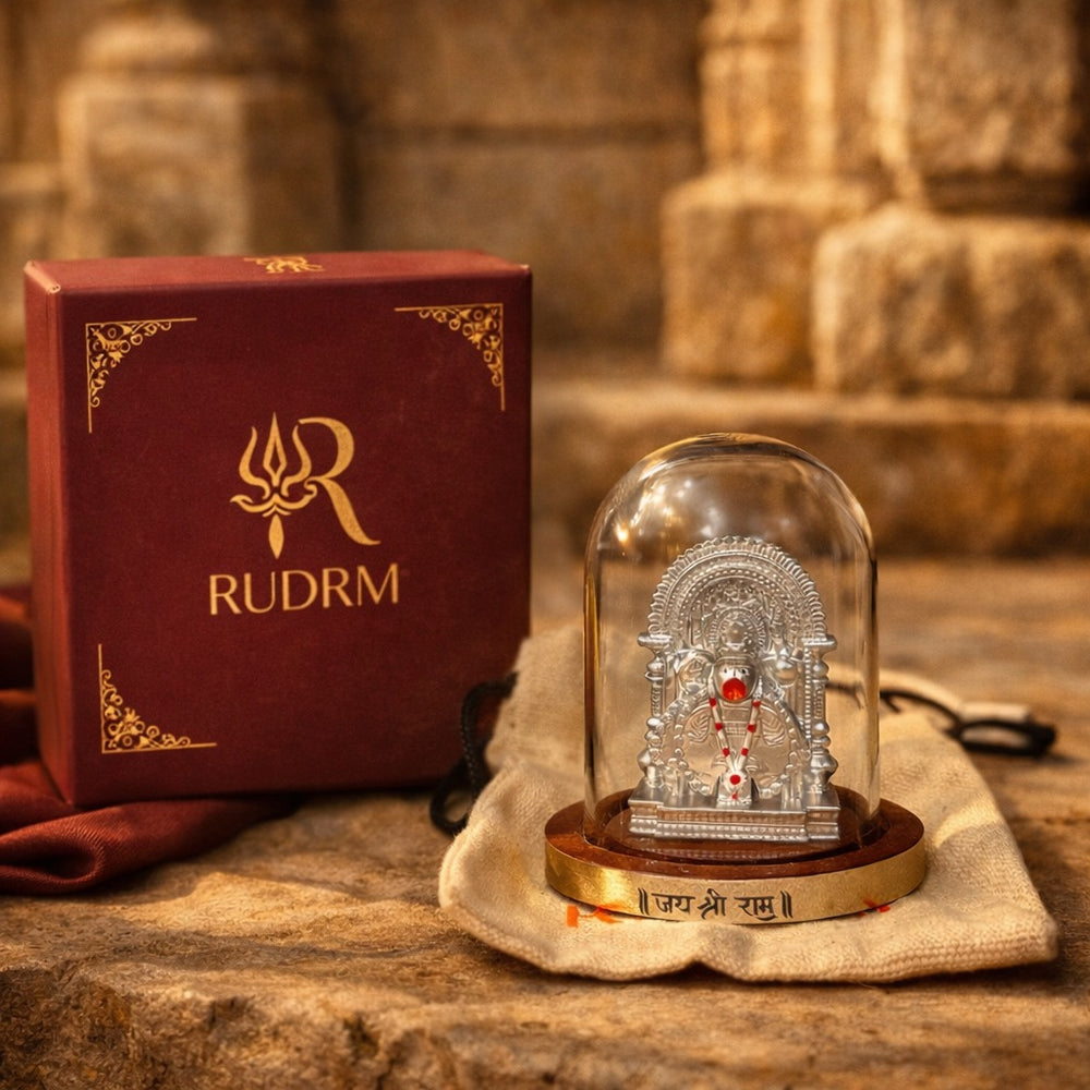 Silver statue of Lord Hanuman under a glass dome with a 'Jai Shri Ram' plaque, placed on a wooden base, next to a 'Rudrm' branded box, with a textured background.