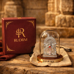 Silver statue of Lord Hanuman under a glass dome with a 'Jai Shri Ram' plaque, placed on a wooden base, next to a 'Rudrm' branded box, with a textured background.
