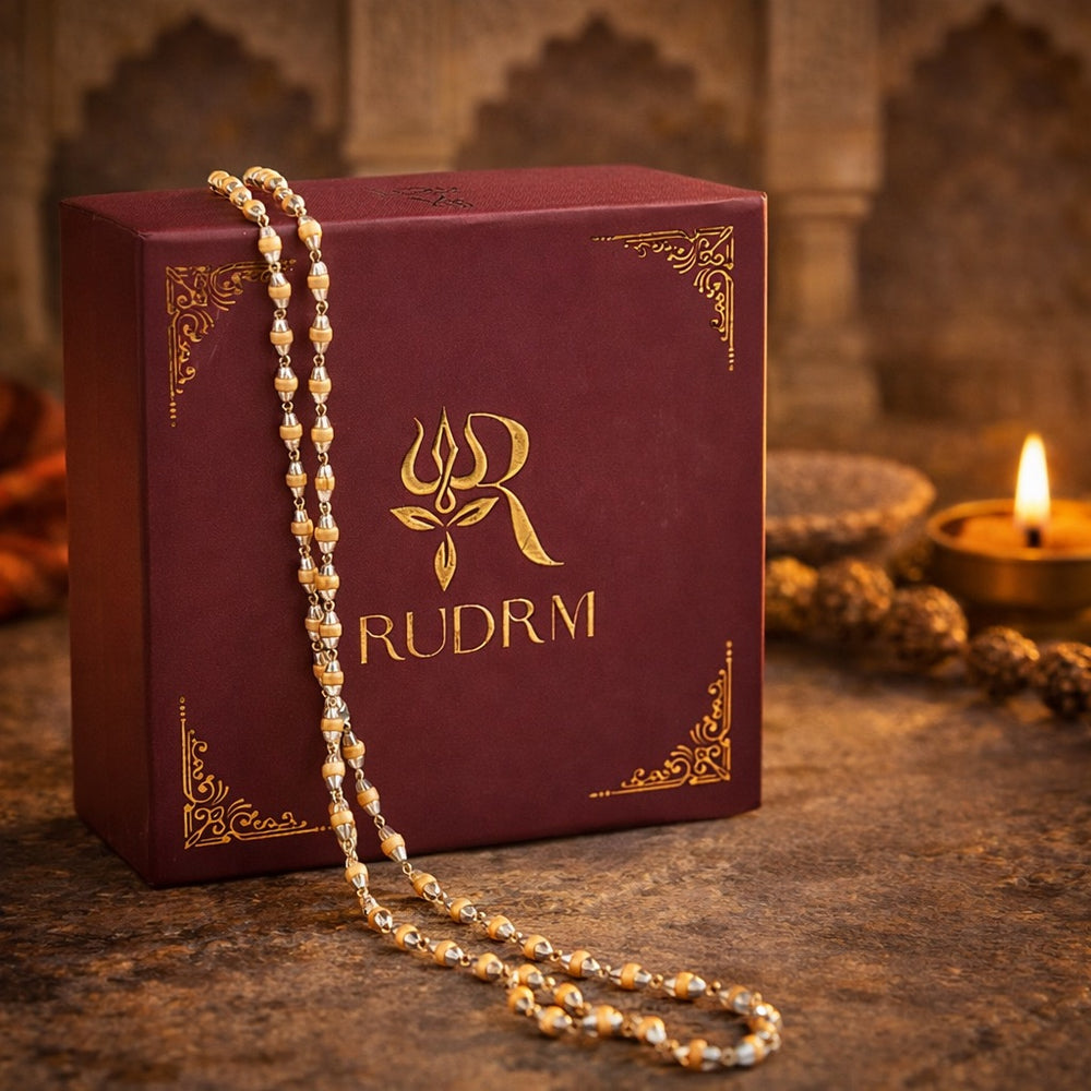 Rudraksha mala necklace placed beside a 'Rudrm' branded box, with a lit diya in the background and textured stone surface.