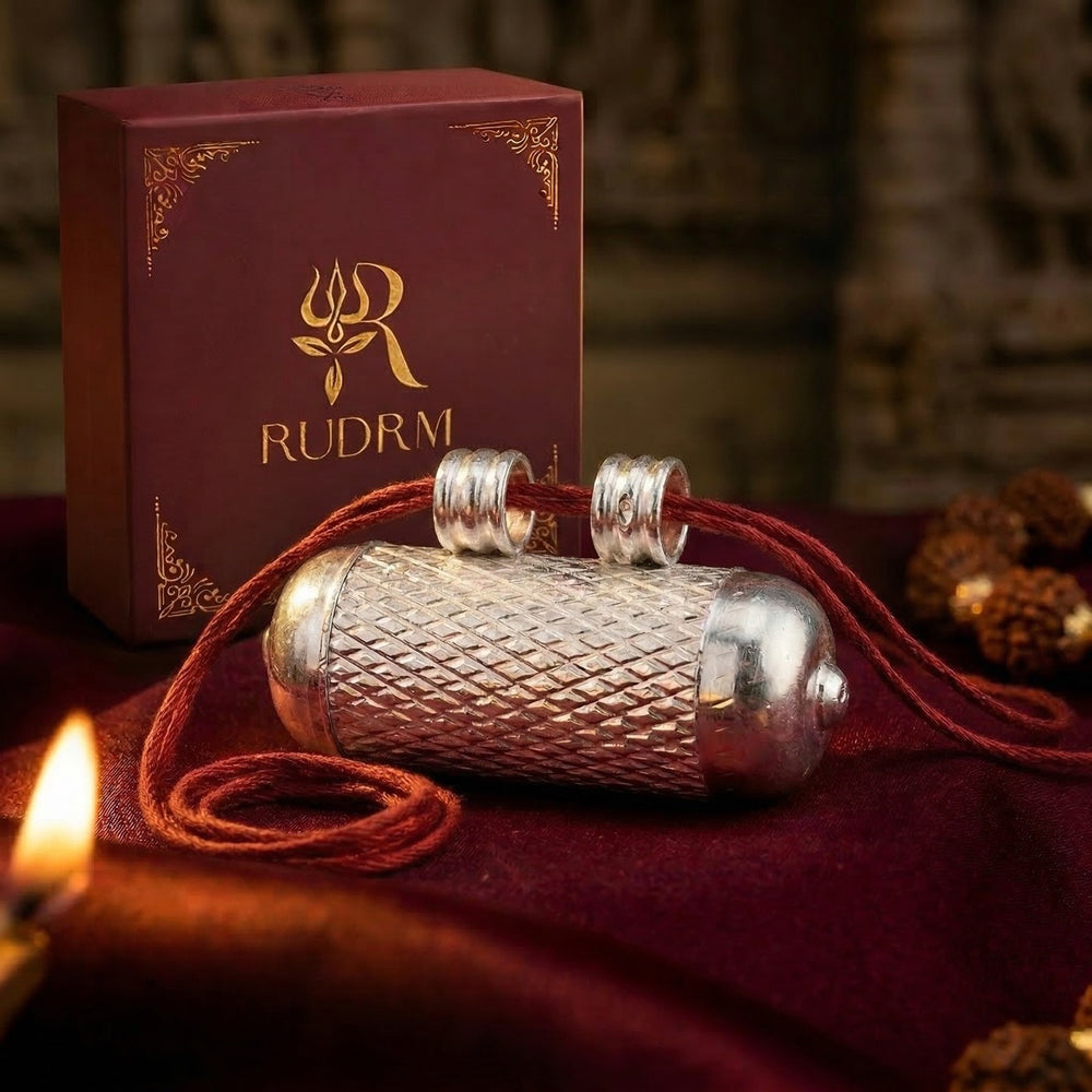 Silver Hanuman Gada pendant with red string, placed next to a 'Rudrm' branded box, set on a maroon velvet background with a lit diya and rudraksha beads.